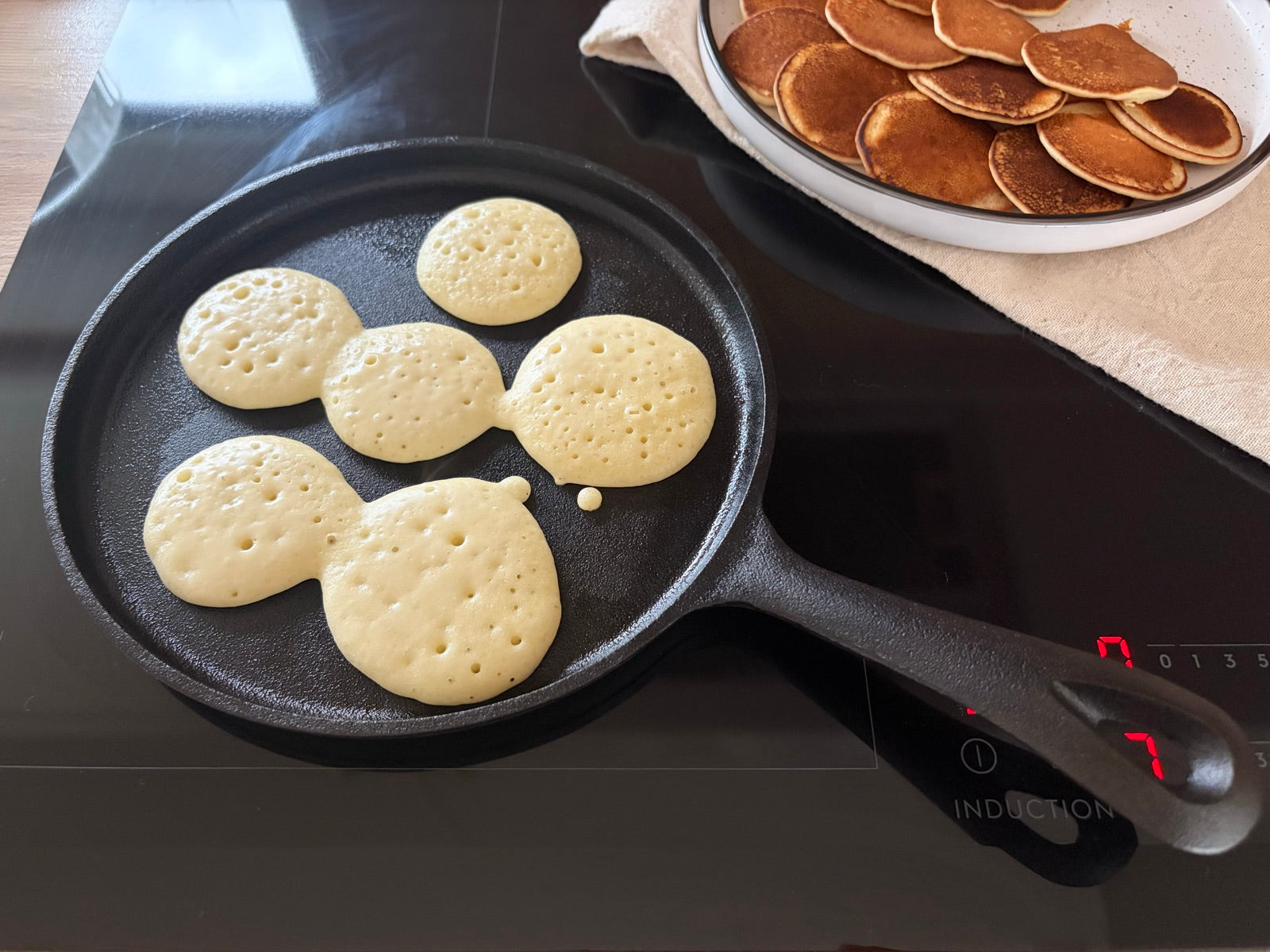 Aluat de mini pancakes pe lespedea de fontă, cu bule la suprafață, gata de întors