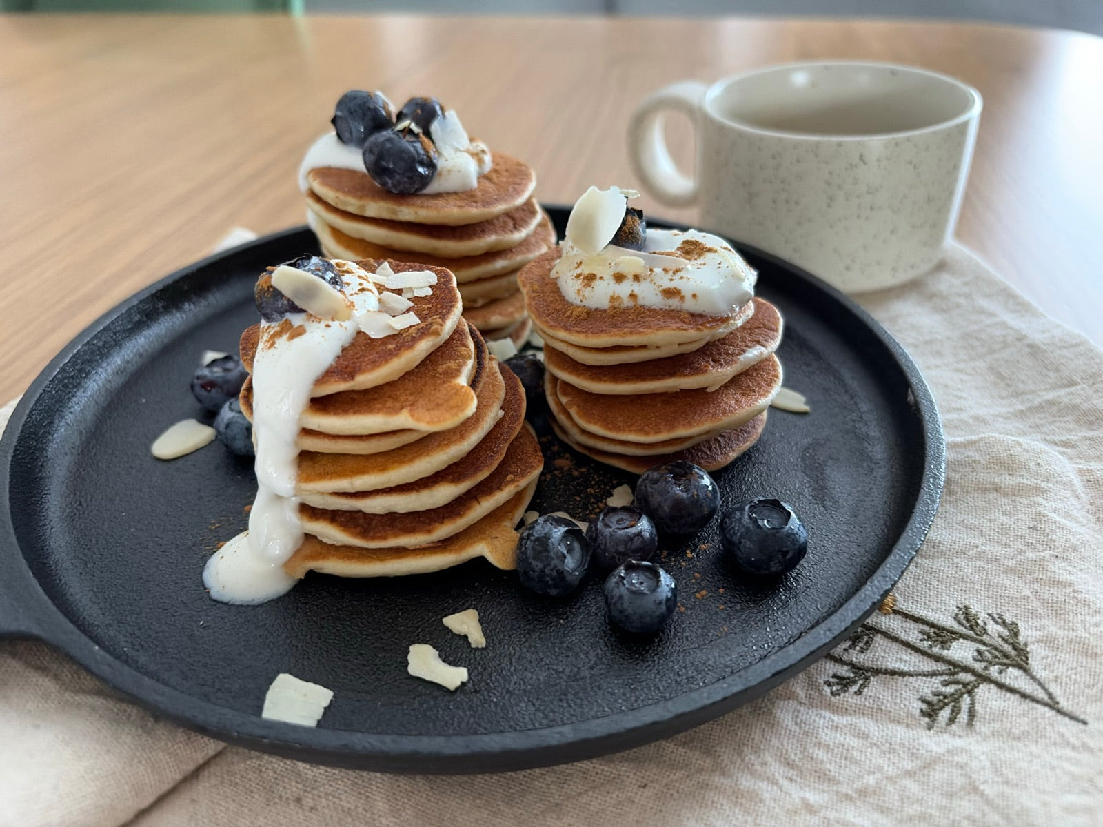 Mini pancakes în teancuri, cu iaurt grecesc, afine, scorțișoară și fulgi de migdale, pe lespedea de fontă